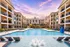 Luxurious apartment complex with modern architecture, featuring a large swimming pool surrounded by sun loungers and beautifully landscaped gardens at sunset.