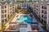 Luxurious apartment complex showcasing a vibrant courtyard with a large swimming pool, surrounded by elegant multi-story buildings and lush landscaping.