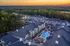 Captivating aerial view of a luxury apartment complex featuring a vibrant swimming pool, surrounded by lush greenery and a serene sunset backdrop.