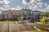 Charming apartment complex with modern architecture, lush landscaping, and ample parking under a bright blue sky.