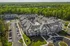 Aerial view of modern apartment complex surrounded by lush greenery, featuring spacious parking lots and a beautifully designed central courtyard with a swimming pool.