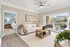 Bright living room with a modern design, featuring a cozy white sofa, wooden coffee table, and large sliding glass doors opening to a spacious balcony with a garden view.