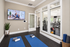 Inviting yoga room featuring blue mats, a wall-mounted screen, and a serene view into a modern fitness area with state-of-the-art equipment.