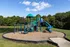 Charming playground with vibrant blue and green slides, surrounded by lush greenery and clear skies, ideal for family fun.