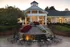 Elegant clubhouse entrance with illuminated windows, surrounded by lush gardens and inviting outdoor seating area.