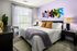 Bright and cozy bedroom with stylish decor, featuring a colorful abstract wall art, plush bedding with warm accents, and natural light streaming through a large window.