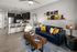 Modern open-concept living room and kitchen with elegant dark cabinetry, cozy blue sofa, stylish decor, and chic hanging lights.