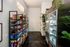 Modern apartment amenity featuring a bright snack station with neatly organized shelves of vibrant products and sleek glass refrigerators, surrounded by lush greenery.
