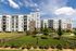 Modern apartment building with spacious balconies and lush green landscaped grounds under a bright blue sky.