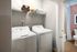 Modern laundry room with sleek washer and dryer, ample shelving space, and an adjacent bathroom view.