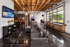Modern entertainment room with a cozy gray couch, arcade games, and a TV displaying a basketball game; features industrial-style d&eacute;cor with exposed wood beams and large windows.