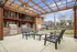 Inviting outdoor patio with modern pergola, stylish seating, and dual stainless steel grills set against a charming brick backdrop, perfect for entertaining.