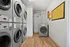 Modern apartment laundry room featuring stacked stainless steel washers and dryers with efficient wood-style flooring.
