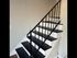 Modern staircase with sleek black and white steps and elegant metal railing, connecting to warm wooden flooring.