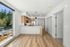 Bright modern kitchen with sleek countertops, pendant lighting, and wood accents, featuring a scenic view of lush greenery through large windows.