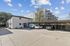 Charming two-story apartment building with a spacious parking area, surrounded by lush greenery and clear blue skies, offering a cozy neighborhood vibe.