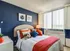 Inviting bedroom with navy accent wall, vibrant pillows, and ample natural light.
