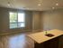 Bright and spacious living area with modern hardwood flooring, large window offering natural light, and a sleek kitchen island with sink.