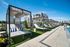 Elegant poolside cabanas with striped pillows under a clear blue sky, set beside a modern apartment complex.