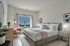 Beautifully designed bedroom featuring a plush bed, pink accent chair, modern decor, and a window with a scenic view.