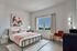A bright and modern bedroom with a stylish metal bed frame, colorful artwork, and serene window view.