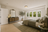 Elegant bedroom featuring a cozy bed with soft linens, a stylish dresser with a mirror, and abundant natural light from large windows with lush greenery outside.