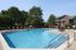 Inviting outdoor pool area with comfortable loungers, surrounded by lush greenery and modern apartment buildings.