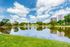 Scenic view of serene lake with lush greenery, surrounded by modern apartment buildings under a vibrant blue sky.