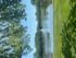 Serene lakeside view with a tranquil fountain surrounded by lush greenery under a clear blue sky.