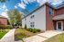 Charming brick and siding apartment exterior with lush landscaping and a clear blue sky, inviting community walkway.