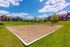 Inviting sand volleyball court surrounded by lush green lawns and picturesque apartments under a bright blue sky.