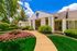 Elegant apartment entrance surrounded by vibrant landscaping, showcasing a welcoming curb appeal under a bright blue sky.