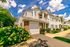 Charming townhouse with a blend of brick and siding exterior, surrounded by lush greenery and vibrant flowers under a bright blue sky.