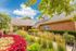 Charming brick apartment building surrounded by lush greenery and vibrant flower beds under a clear blue sky.