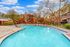 Inviting outdoor pool area with elegant sun loungers, surrounded by charming brick apartment buildings and lush trees under a bright blue sky.