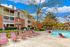 Inviting apartment complex with a charming brick exterior and lush greenery, featuring a sparkling swimming pool surrounded by comfortable lounge chairs, perfect for relaxation.