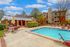Inviting outdoor pool area with cozy seating, lush greenery, and a charming red brick building surrounded by vibrant trees.