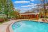 Inviting outdoor pool area with crystal-clear water, surrounded by lush greenery and a charming brick pavilion under a bright blue sky.