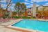 Inviting apartment complex with a crystal-clear pool, surrounded by lush greenery and comfortable lounge chairs, perfect for relaxation.