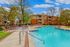 Inviting outdoor pool area with modern lounge chairs, surrounded by lush greenery and stylish apartment buildings under a clear blue sky.