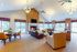 Expansive living room with elegant chandeliers, cozy fireplace, and plush seating, bathed in natural light from large windows.