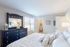 Bright and inviting bedroom with a sleek black dresser, large mirror, and cozy bed adorned with plush pillows.
