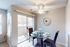 Bright dining area with elegant glass table for two, featuring a stylish ceiling fan and a large sliding door leading to a serene outdoor view.