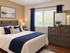 Elegant bedroom with warm tones, featuring a plush bed, cozy blue accents, and a large window inviting natural light.