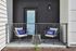 Cozy balcony setup with two wicker chairs, vibrant blue pillows, and a small round table.