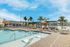 Luxurious outdoor swimming pool area with sun loungers, umbrellas, and palm trees under a clear blue sky.