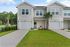 Charming duplex with modern architecture, featuring sleek garage doors and a welcoming front patio set against a backdrop of lush greenery and palm trees.