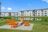 Modern apartment complex with a serene pond view and inviting orange Adirondack chairs around a fire pit, perfect for relaxation and social gatherings.