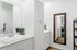 Modern bathroom with sleek white cabinetry, a large mirror, and a stylish sink. A potted plant adds a touch of greenery, enhancing the serene ambiance.