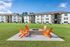 Charming apartment complex with stylish orange chairs around a cozy fire pit, set against a backdrop of lush green lawns and clear blue skies.